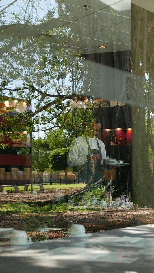Chef in apron holding plates in a cafe window reflection.